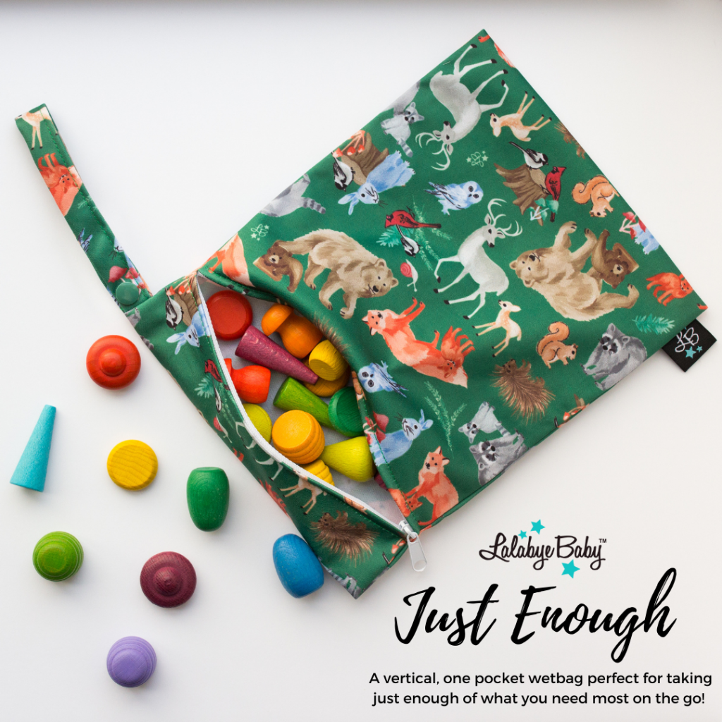 Lalabye Baby Just Enough wet bag. A vertical, one pocket wetbag perfect for taking just enough of what you need most on the go! Image shows a green wetbag featuring woodland animals. The wetbag has a snap handle on the right hand side and has a white zipper closure across the top. Colorful wooden toys are spilling from the wetbag onto the white background beside it.